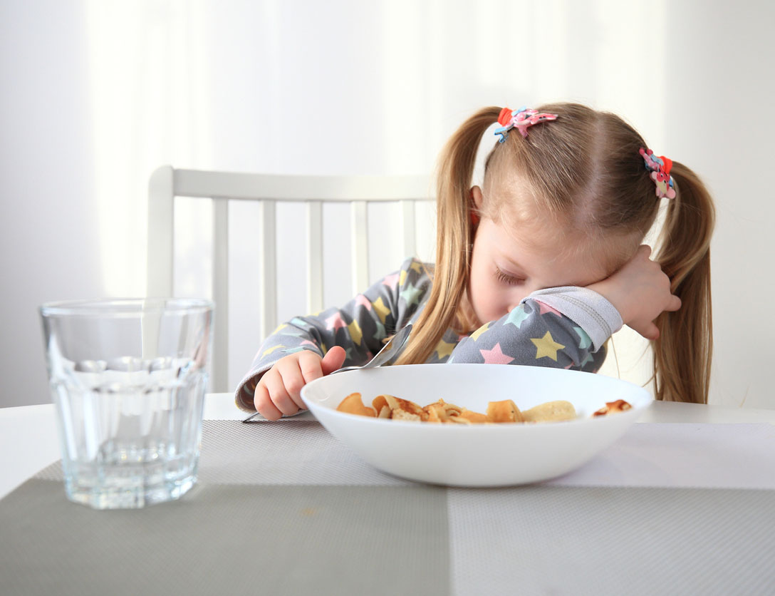 little girl falling asleep at the breakfast table
